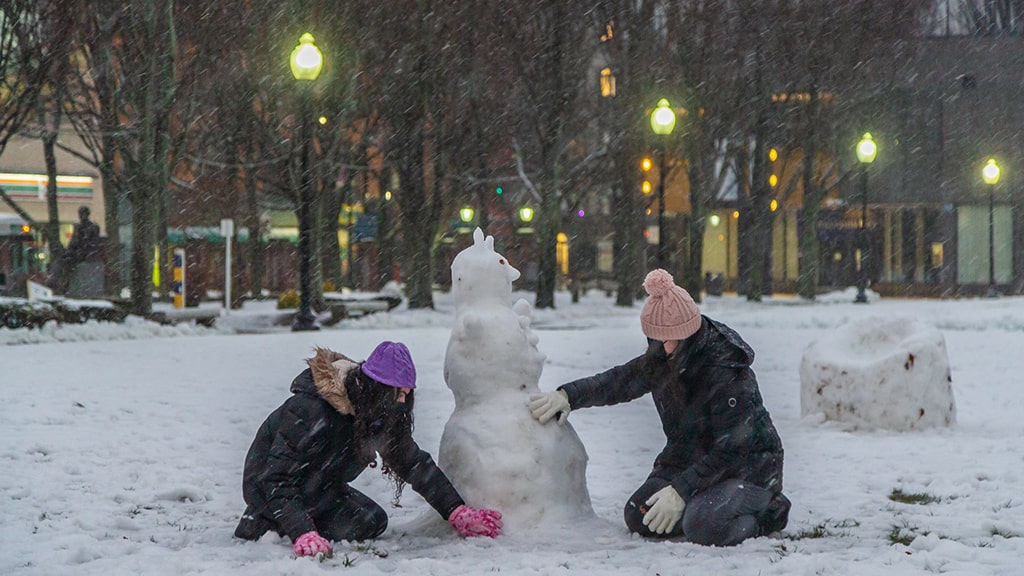 Two students build a snowman in Gaebe commons