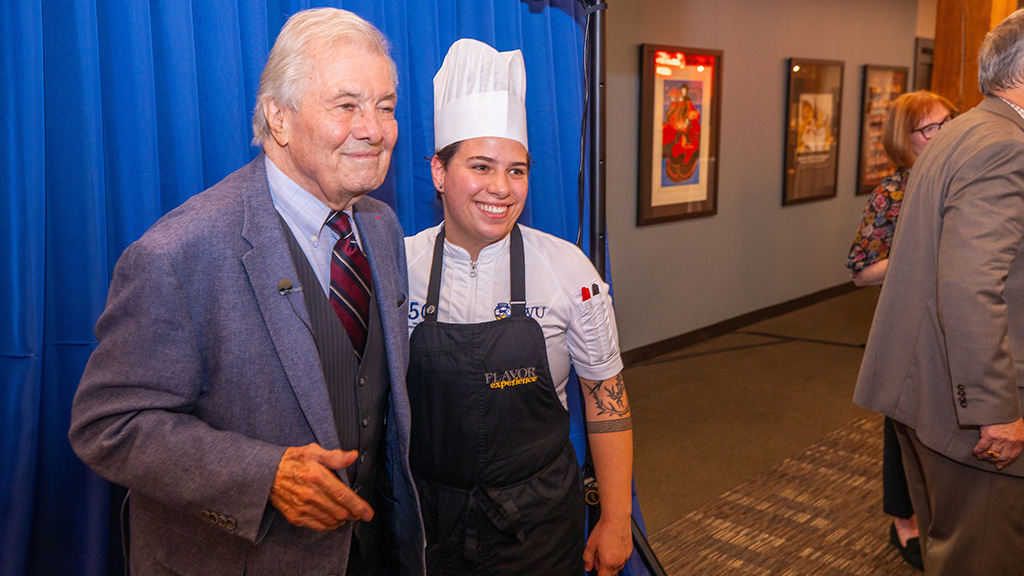 Famous French chef Jacque Pepin and JWU student Rence Loboncz posing for a photo in front of a blue curtain