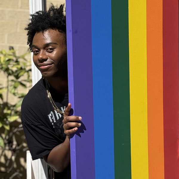 JWU student peering out from behind a Pride flag. 