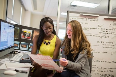Two students discuss advertising project in classroom