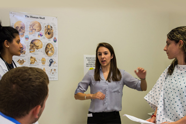 Healthcare administrator talking to physician assistants while a patient listens.