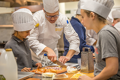 An instructor slices food with a knife as students look on