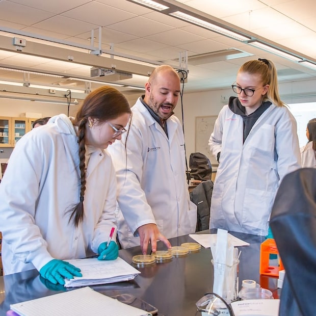 Two students in lab coats with Professor Christos Dimos.