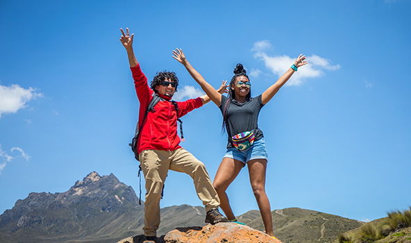 Two students at the top of a mountain raising their hands in the air proud of hiking that far.