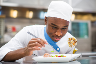 Experiential ed - Male student in chef white plating a dish with tweezers