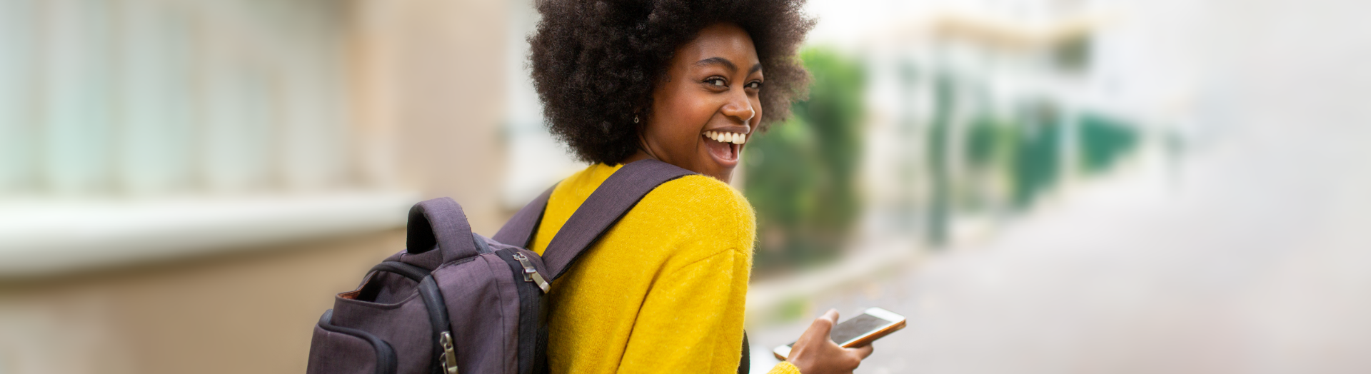 A student looking back smiling while holding a cell phone