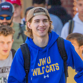 undergraduate application - Undergraduate male student smiling and walking in a crowd of students wearing a JWU Wildcats sweatshirt