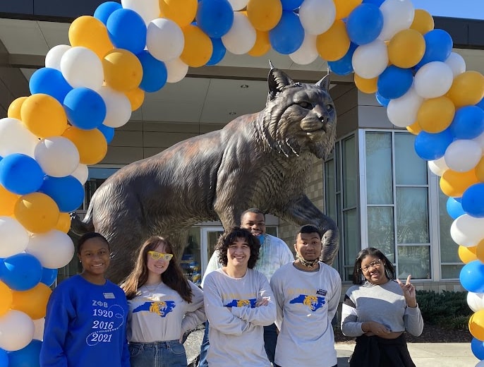 Students standing under a balloon arch in front of the Wildcat statue
