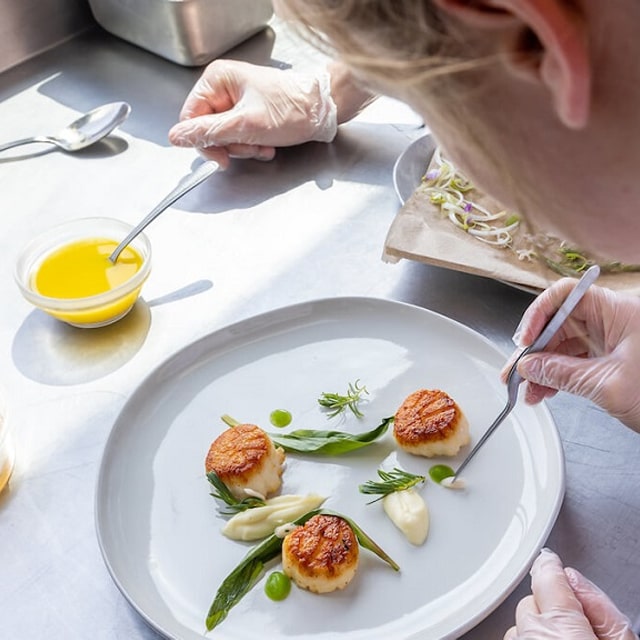 Female culinary student plating fresh scallops.