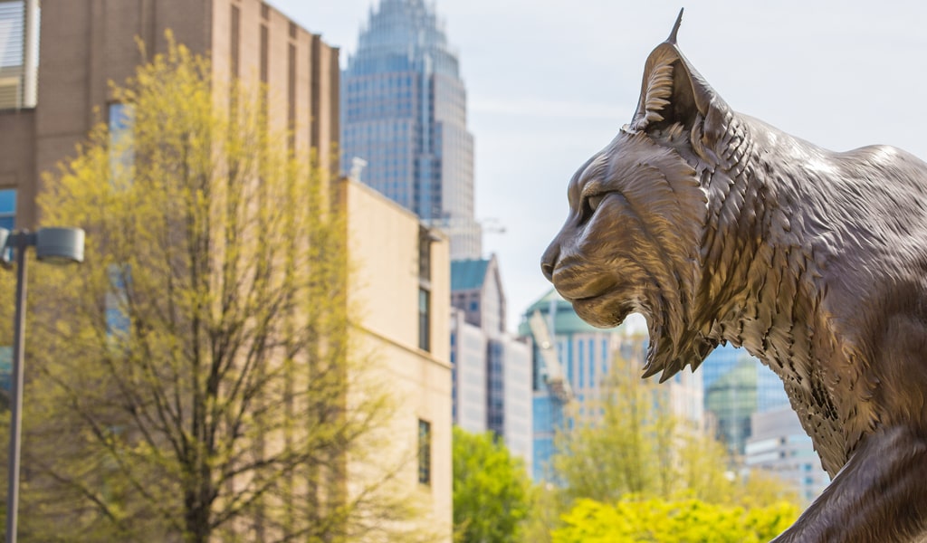 Charlotte Wildcat statue in profile, with city skyline blurred out in the background.