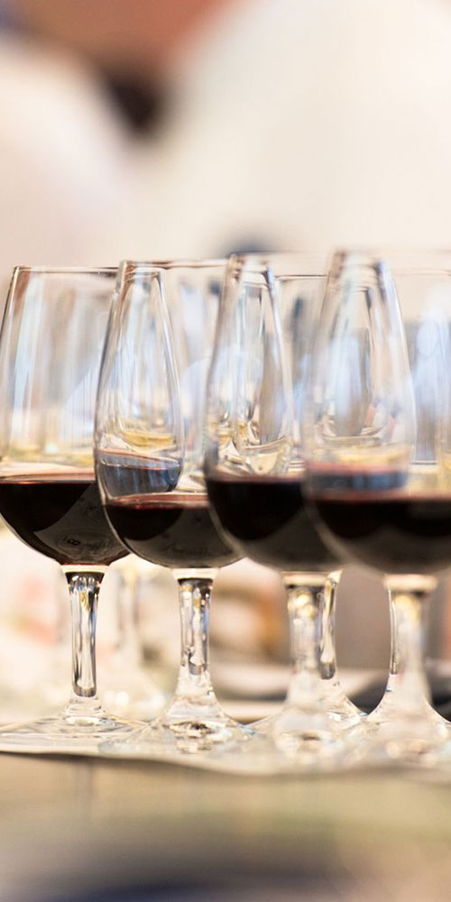 A row of wine goblets filled with red wine. 