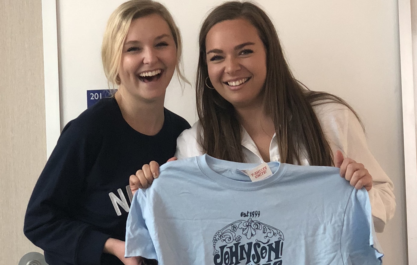 JWU grad Bayla Werman smiling with another student holding up a t shirt