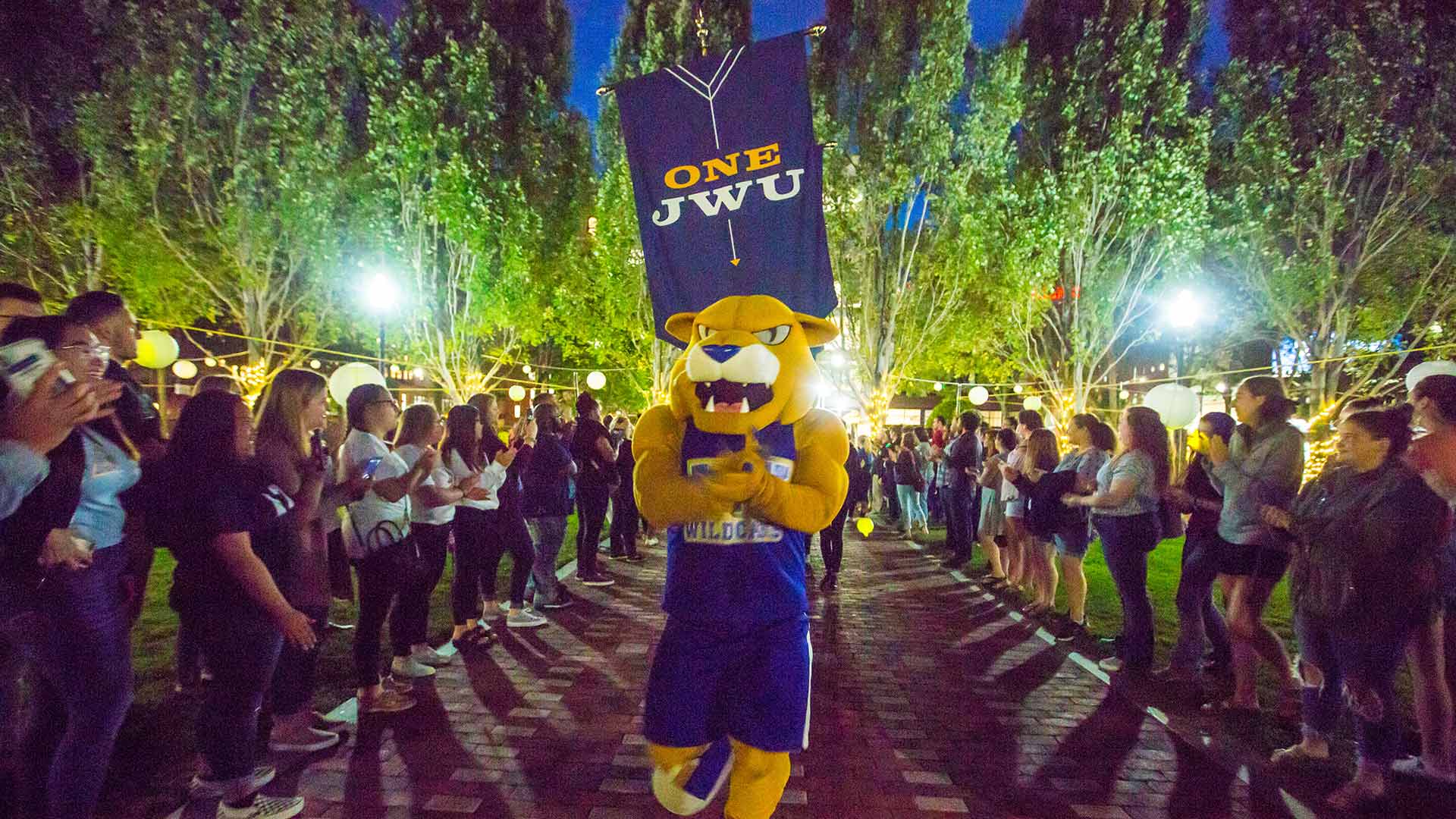 JWU's mascot Willie walks down a pathway lined with students