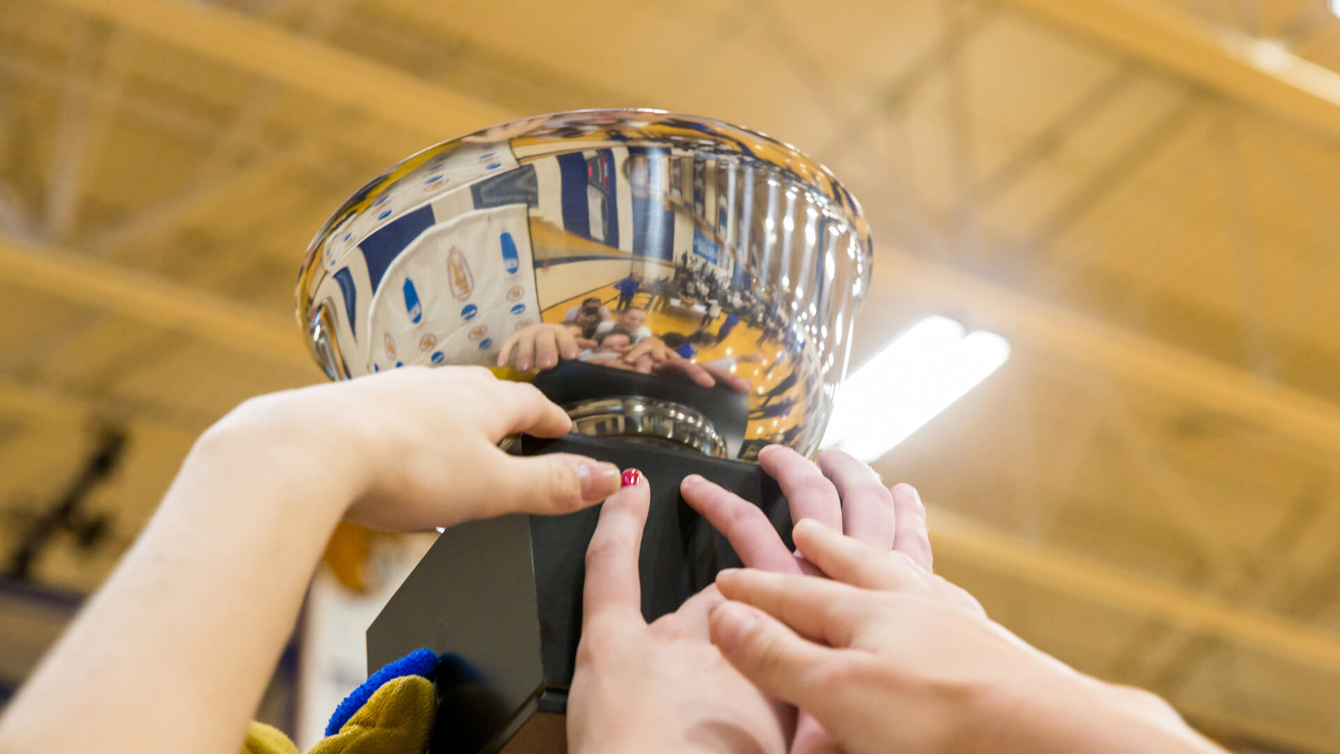 JWU's women's volleyball team holding a trophy up in the air.