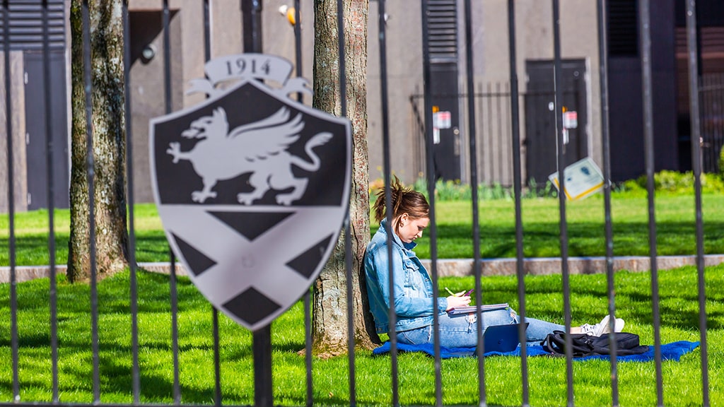 Photo of a student working in Gaebe Commons with JWU gate in foreground