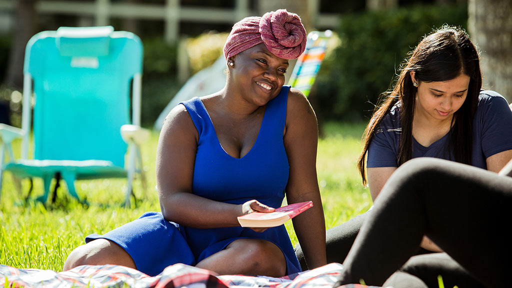 A student and friends sitting outside on a blanket with a book