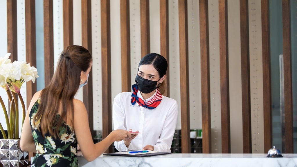 Female hotel employee greets guest with mask