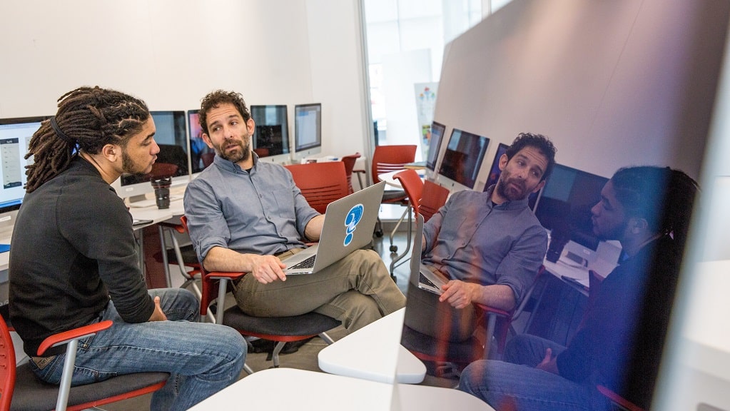 Male faculty and mentee talk in a computer lab.
