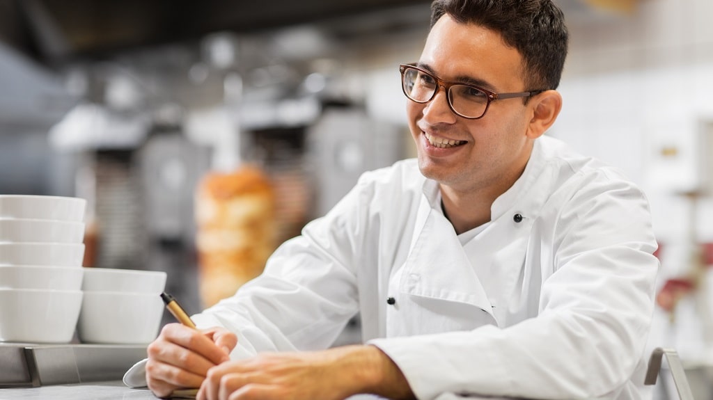 Male chef with glasses smiles in kitchen