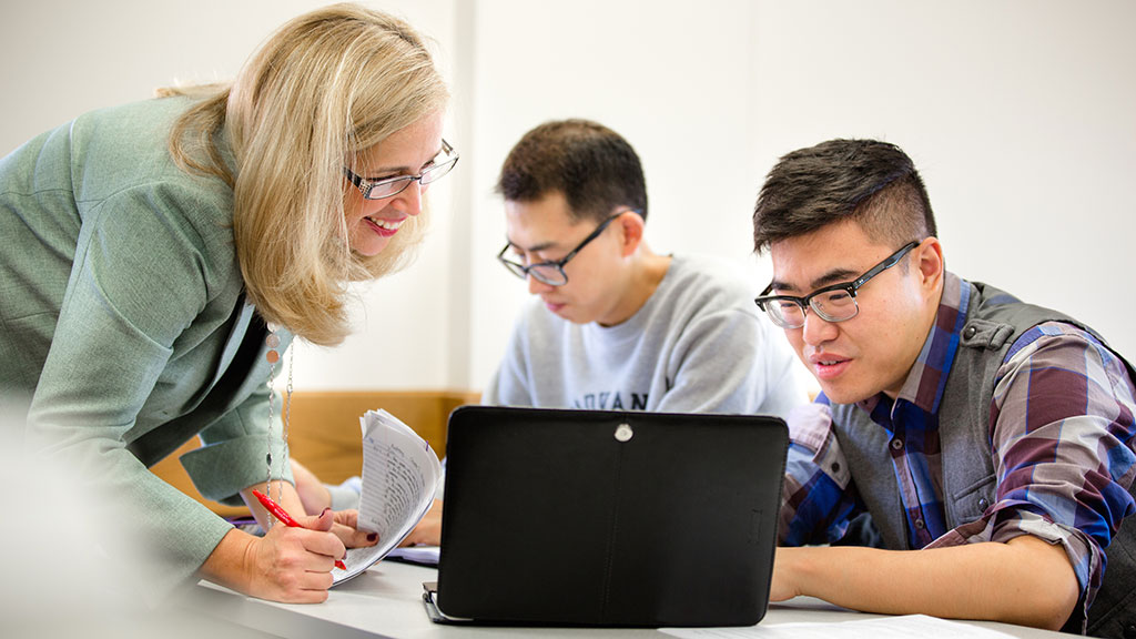 a female instructor and male student smile as they both look at work on the student's laptop