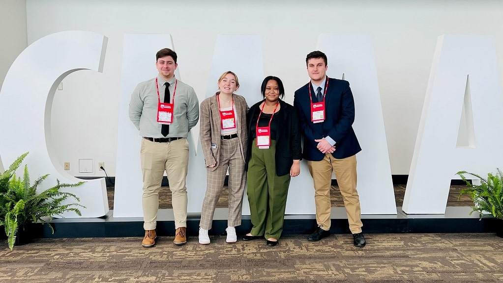 Four JWU students in front of CMAA sign at conference