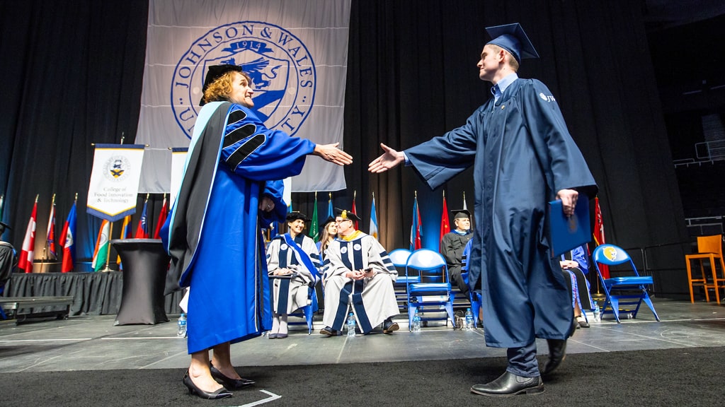 Stage view as a new grad accepts his diploma (and a handshake).