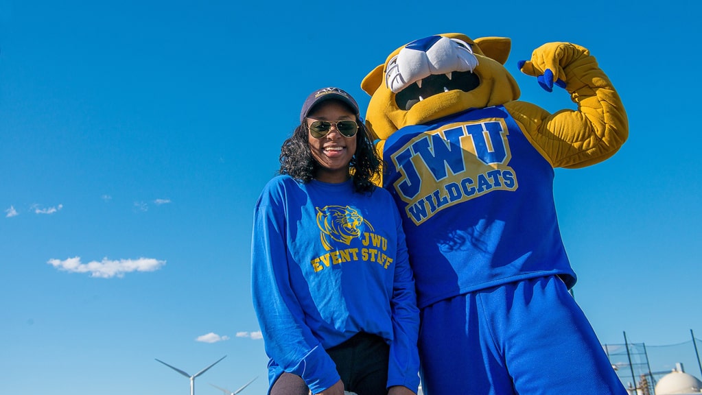 Willy the Wildcat posing with a JWU student with a blue sky backdrop.