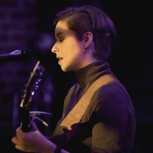 action shot of Ashlynn Kirrane '25 singing and playing guitar on stage