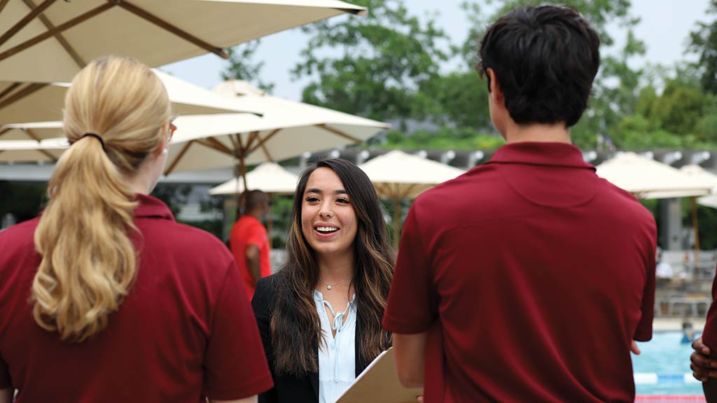 Madison Allan '23 is photographed holding a clipboard and giving directions to other interns, all in matching red polos, at her internship site