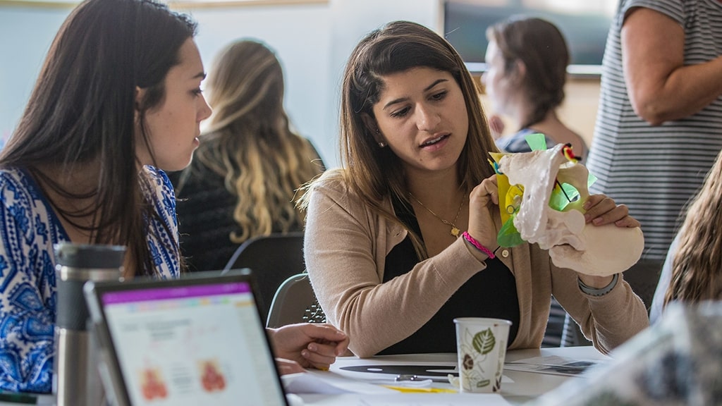 Female students in a science class look at a skeleton