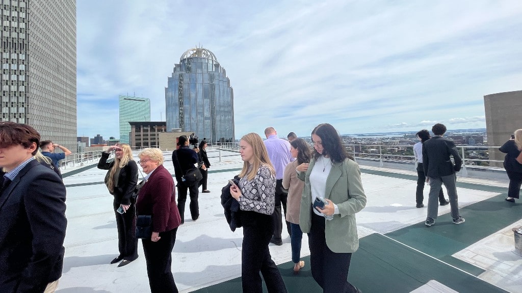 Class standing on top of building with Boston skyline