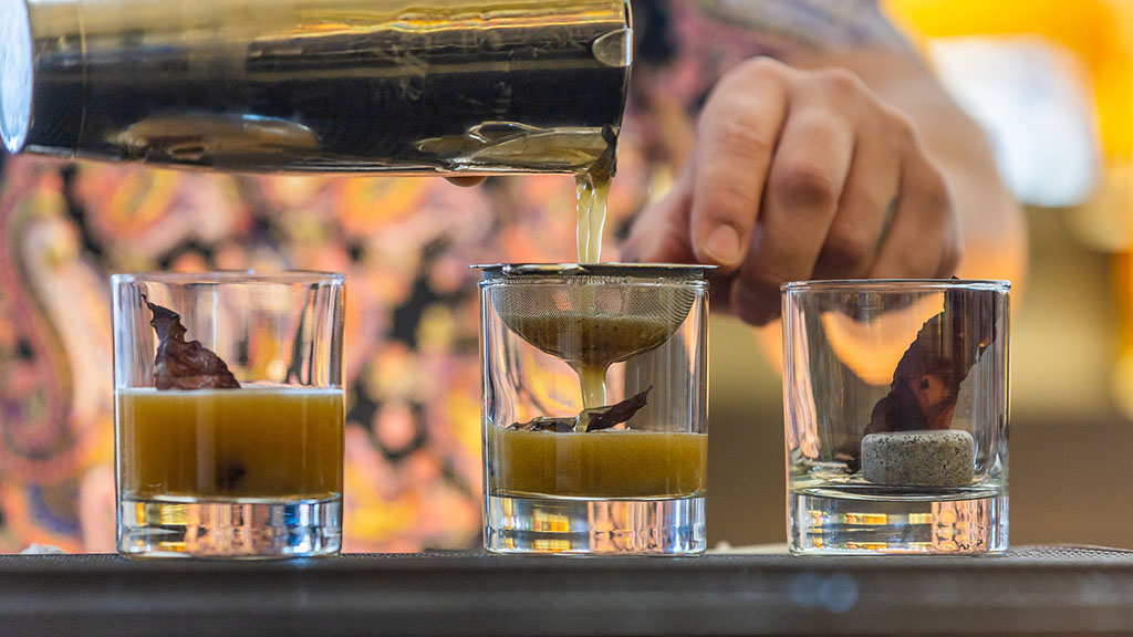 Three glasses of the Boston Stone drink being poured through a strainer