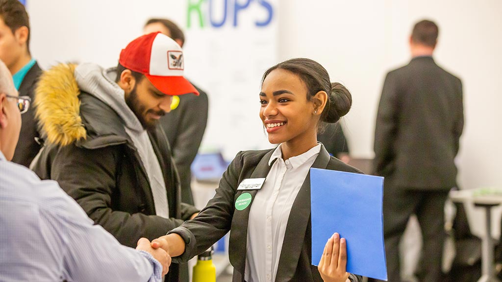 a JWU student shakes the hand of a potential employer while wearing an "internship ready" sticker