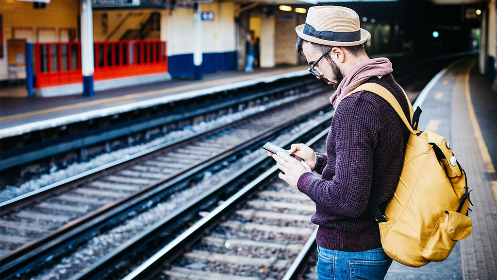 Traveler stands by train tracks, checking phone