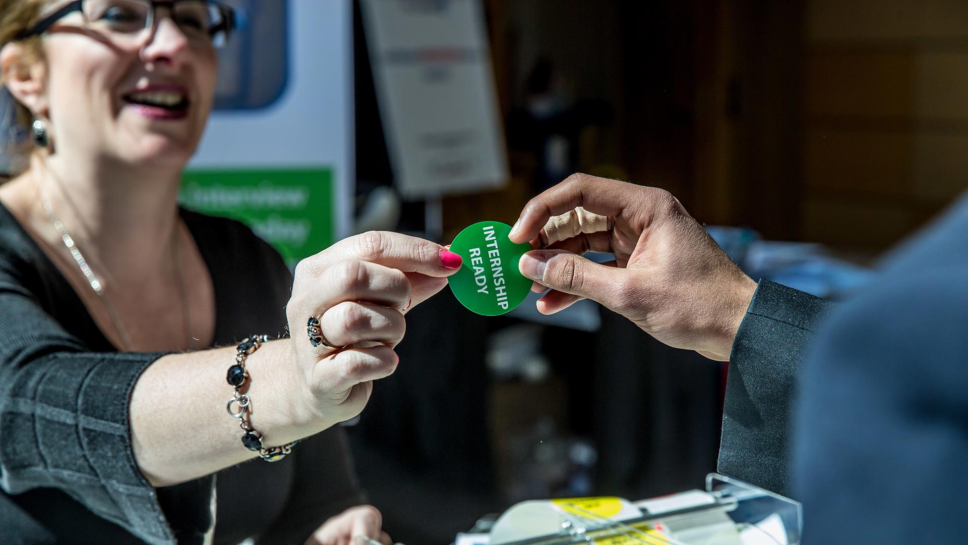 closeup photo of a green sticker saying "internship ready" that a woman is handing out to someone