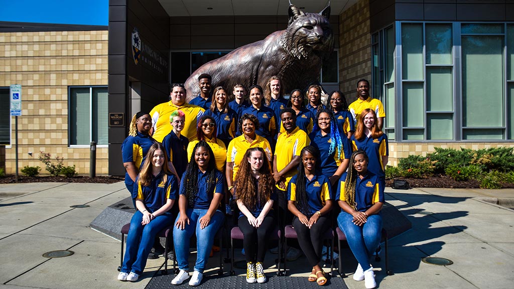 Members of JWU Charlotte's Residence Life team gather in front of a statue of Willie the Wildcat