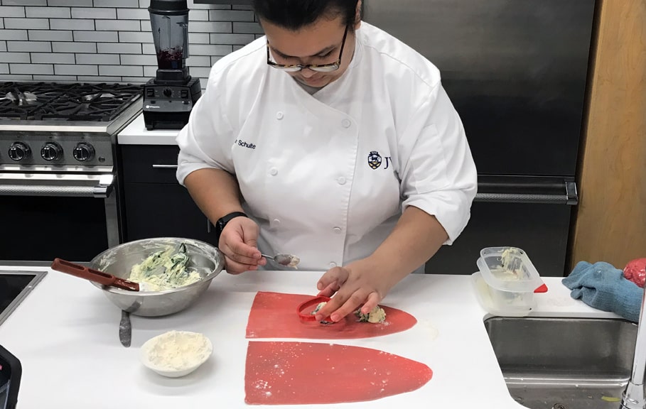 JWU Providence culinary student Meghan Schulte cutting heart-shaped ravioli out of sheets of pasta.