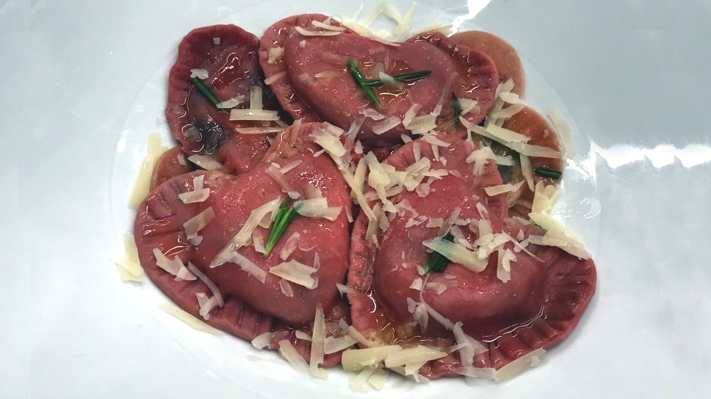 Finished plate of heart-shaped ravioli with brown-butter sauce and a dusting of Parmesan on top.