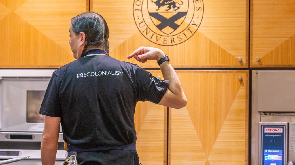 Chef Sean Sherman points to the #86Colonialism slogan printed on the back of his t-shirt.