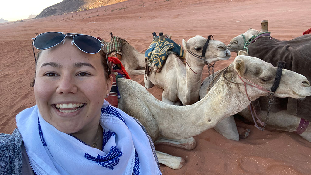 JWU student Teagan Nine in front of camels in Jordan