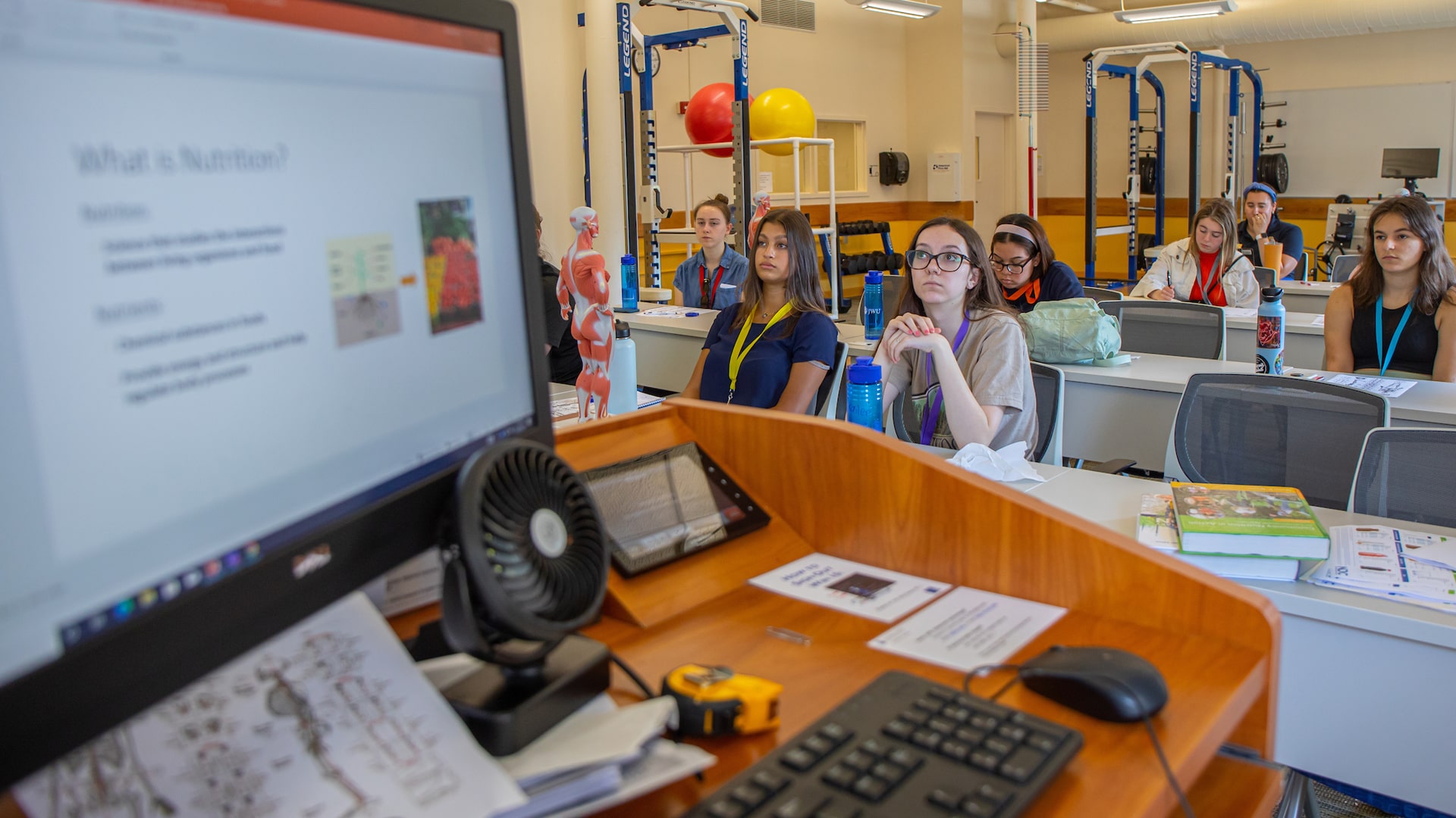 Students facing the front of a classroom with a computer screen flashing, “What Is Nutrition?”