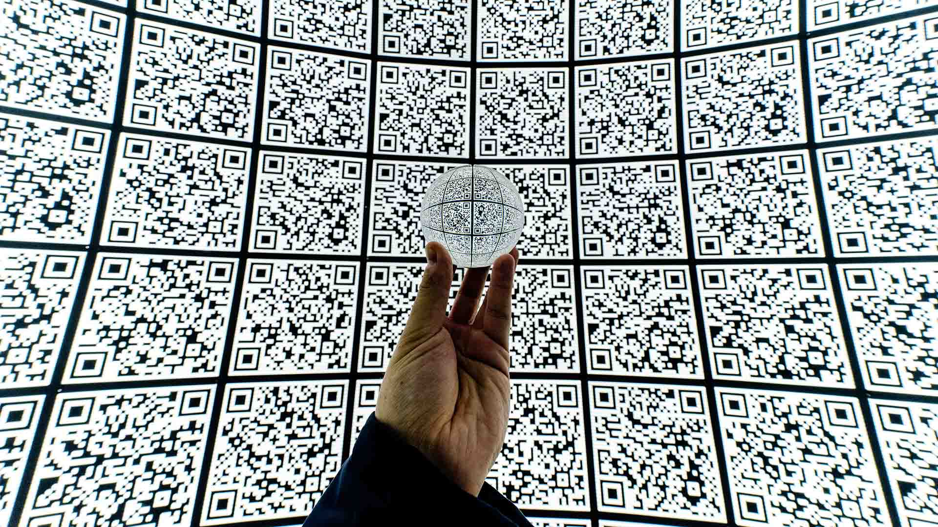 A wall of QR codes with a hand holding a glass ball 