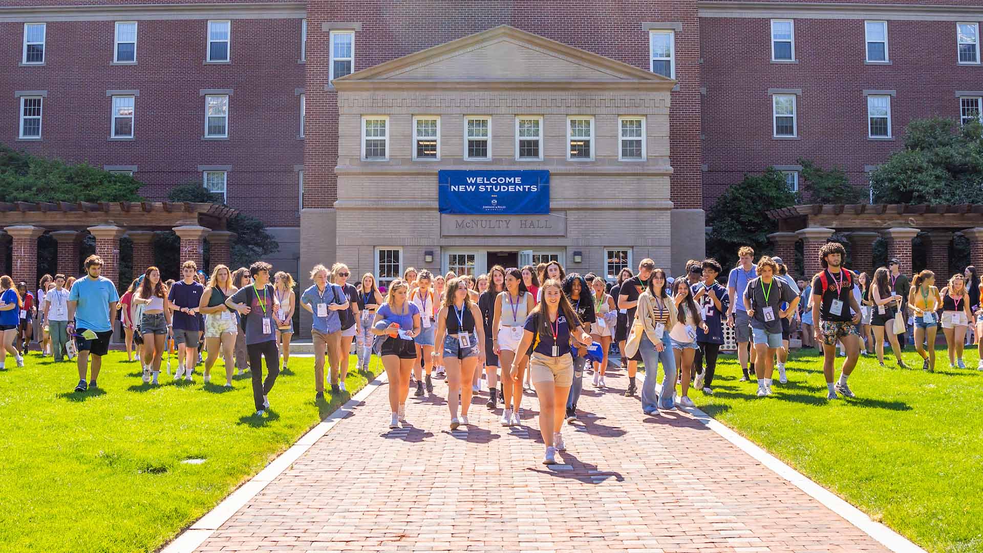 JWU students walking in Gaebe Commons with a sign behind them that reads "Welcome New Students"