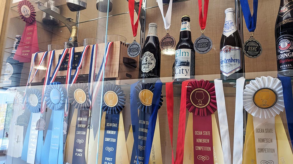 a photo of one shelf of a multi-shelf display full of ribbons and medals won at beer and mead competitions