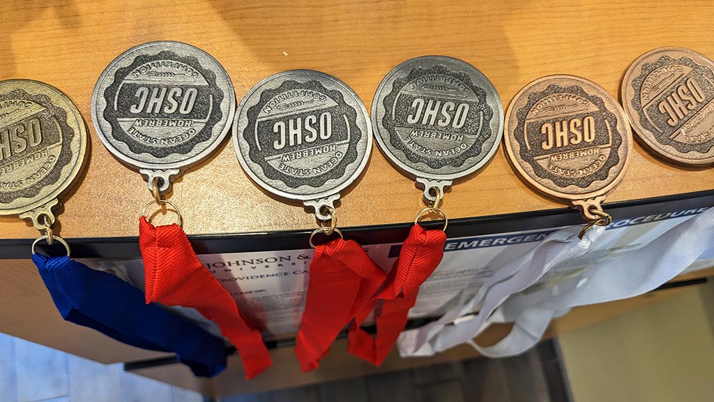 a closeup photo taken from a above of a line of six medals won at the Ocean State Homebrewing Competition