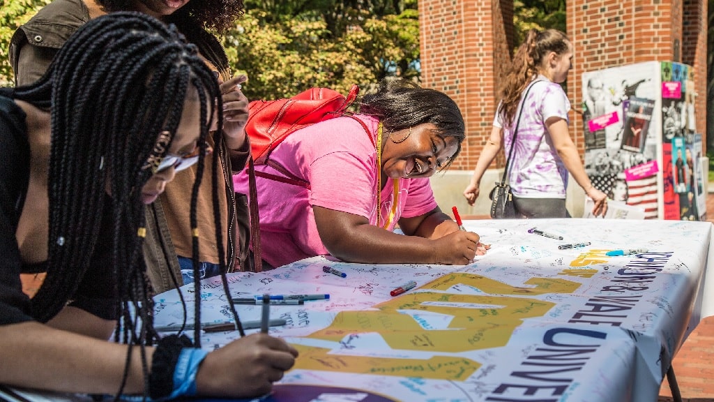 Two jwu students signing a banner 