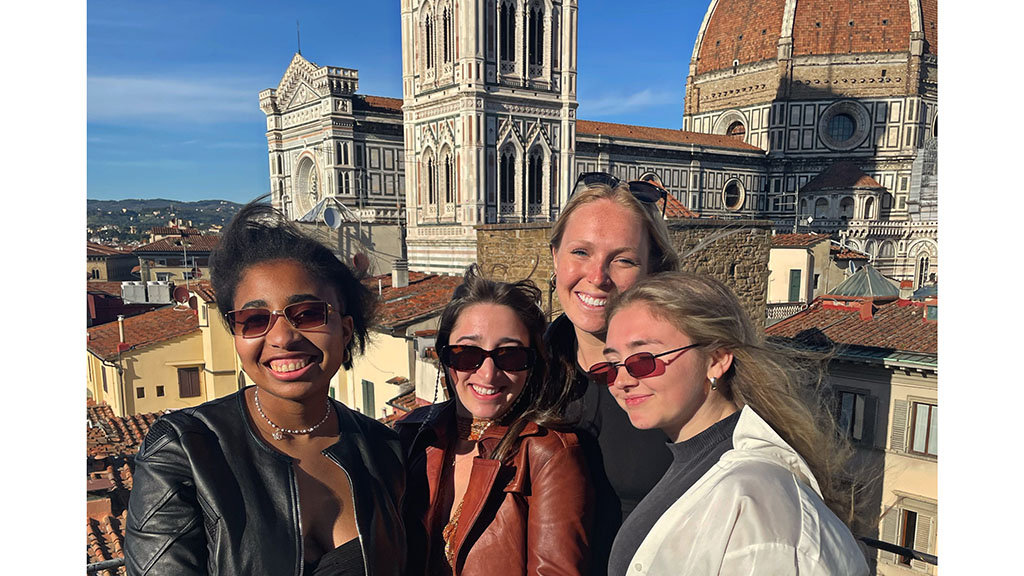 Four girls standing on a balcony in Italy with buildings behind them