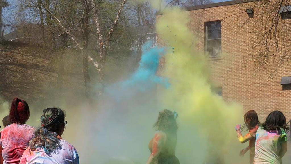 group of students swirling yellow and blue chalk powder into the air