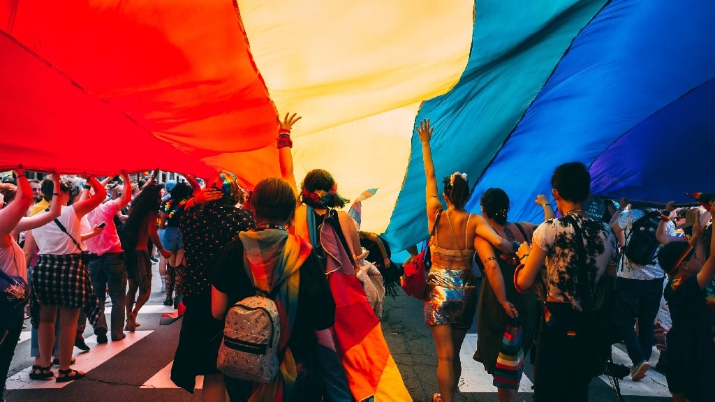 people under a rainbow parachute at a pride festival 