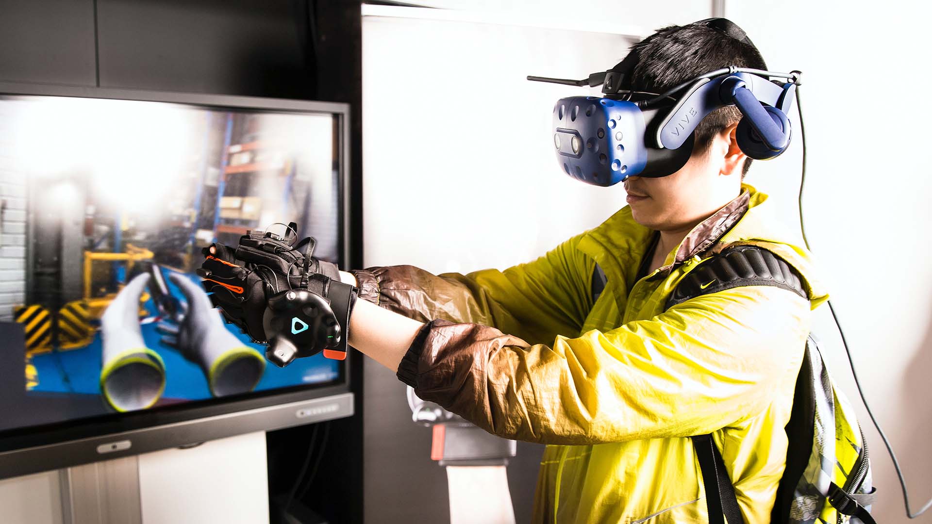 A man using a virtual reality headset with a screen behind him.